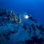 diver holding flashlight swims over a sunken shipwreck