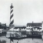 a diagonally striped lighthouse at the water's edge